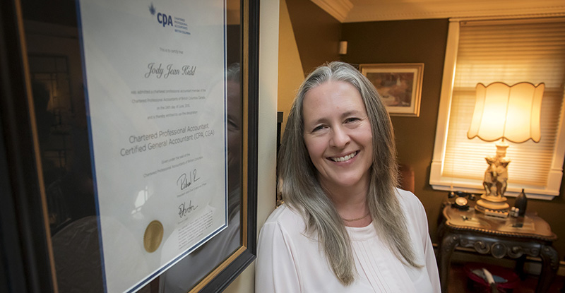 Jody posing with her CPA diploma on the wall behind her