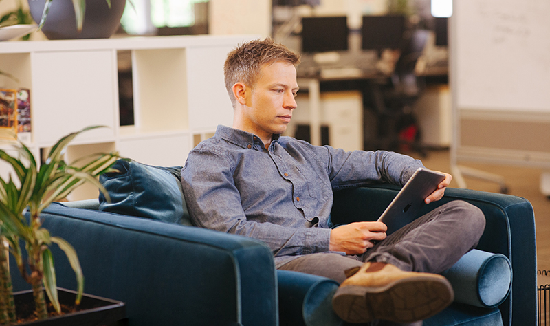 Jeff Wasyliw working on his iPad while sitting in an armchair in the Alida office