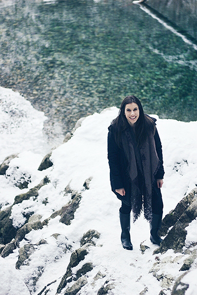 Tiana Tomasetti looks up to the camera standing on a snowbank with a winter scene behind her