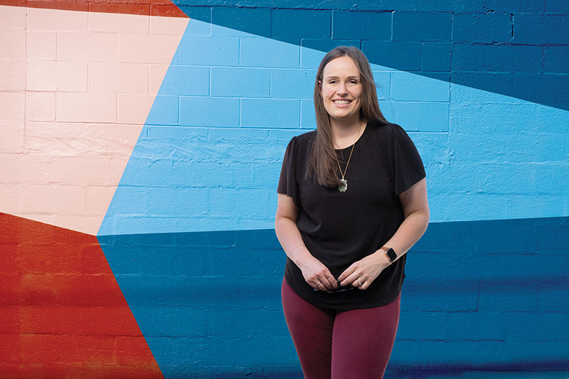 Rhian Quarry, C P A, poses in front of a mural by Pablo Zamudio in East Vancouver and smiles at the camera