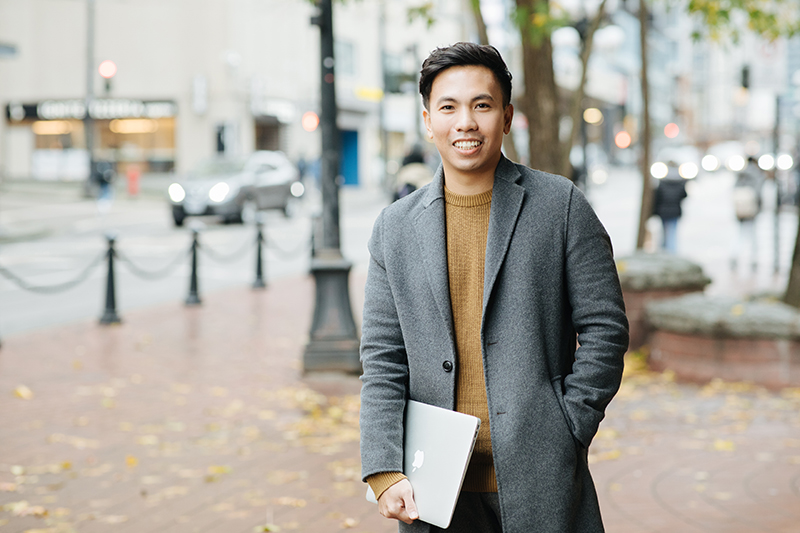 Tony Huynh, holding a laptop and standing in front of a lamp post in Gastown