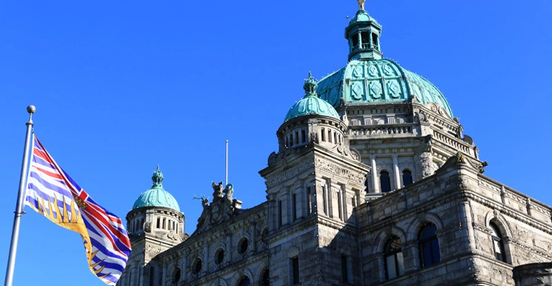 Image of the legislature building in Victoria with a BC flag flying in front