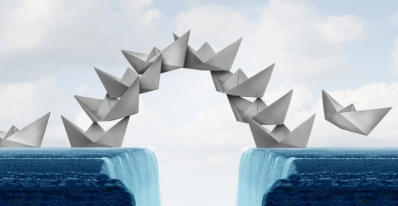 Paper boats symbolizing people working together to form a bridge over a gap between two waterfalls