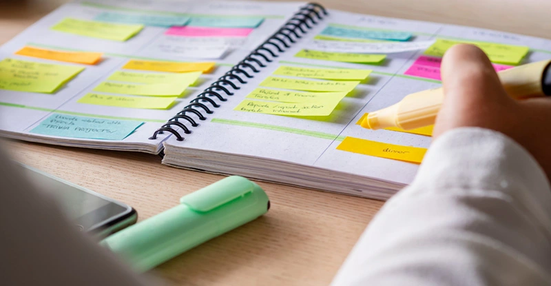 Person working in a day timer with sticky notes and highlighters