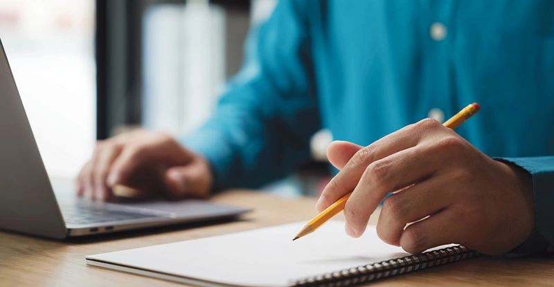 A man is writing on a notebook with a pencil