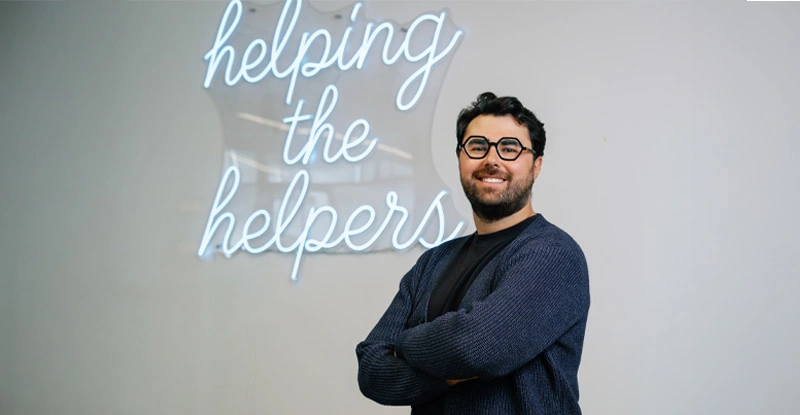 Josh Andler standing in front of a "helping the helpers" light sign