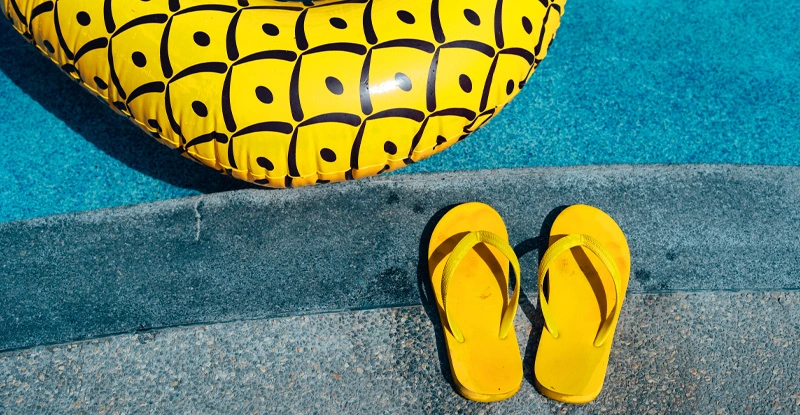 Yellow flip flops sitting on the edge of a pool with a yellow inflatable tube in it