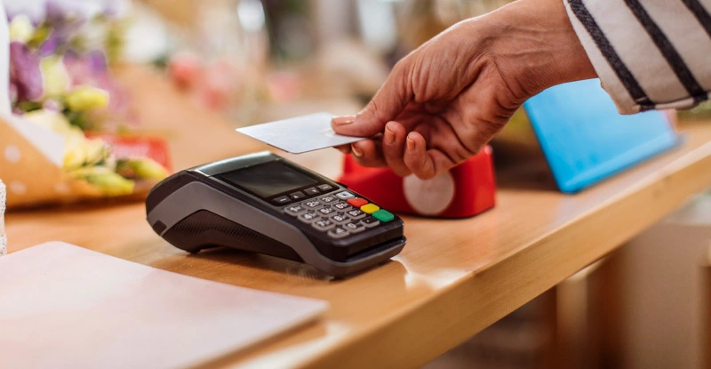 Hand tapping a credit card on a card reader on a desk