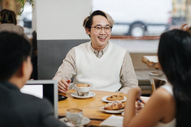 Tony Huynh, Frederick Wong, and Karina Pangilina enjoying coffee and treats while gathered at a table in a cafe, with  Frederick in the centre